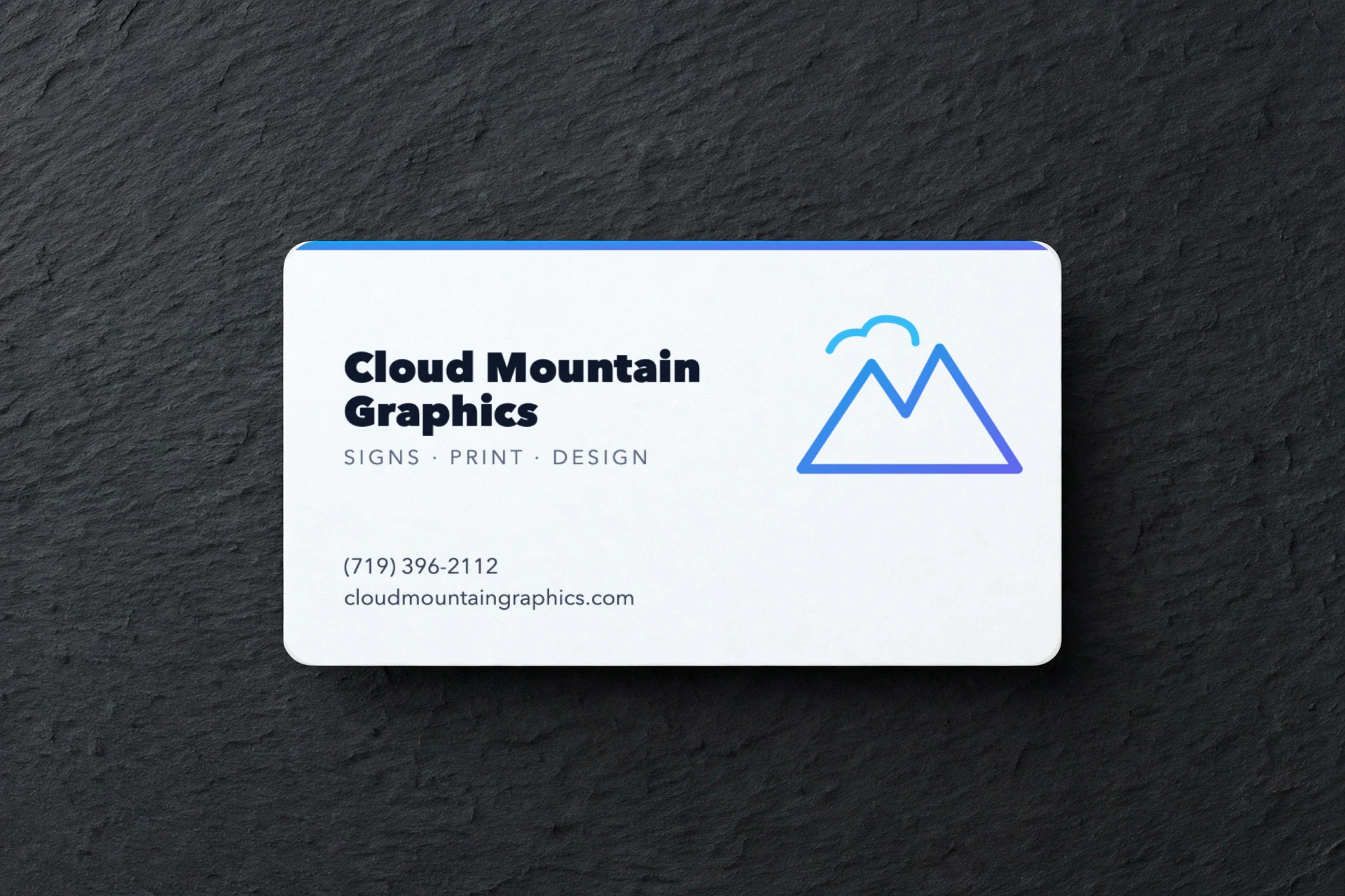 White business card with an azure mountain mark, flat on a slate surface