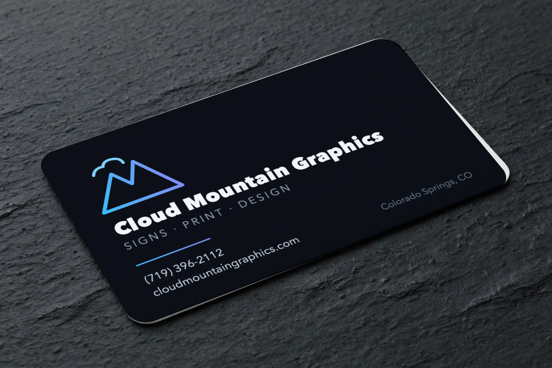 Printed business card, dark design with azure mountain mark, on a slate surface