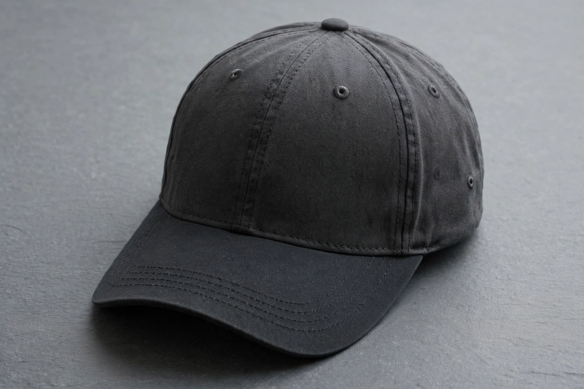 Plain dark charcoal six-panel cap on grey slate