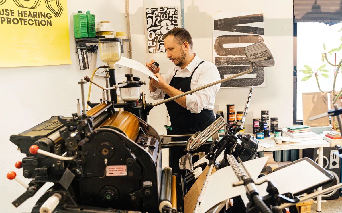 A press operator checking a freshly printed sheet mid-run