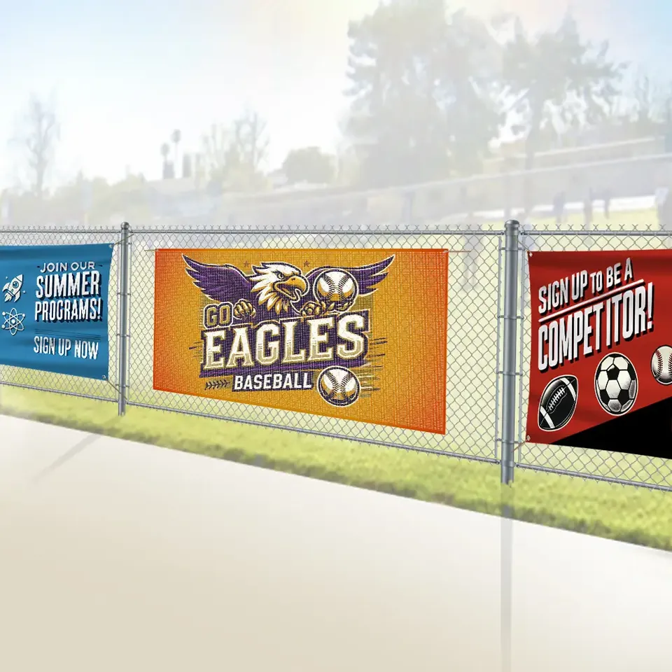Printed banners zip-tied along a chain-link fence beside a ball field