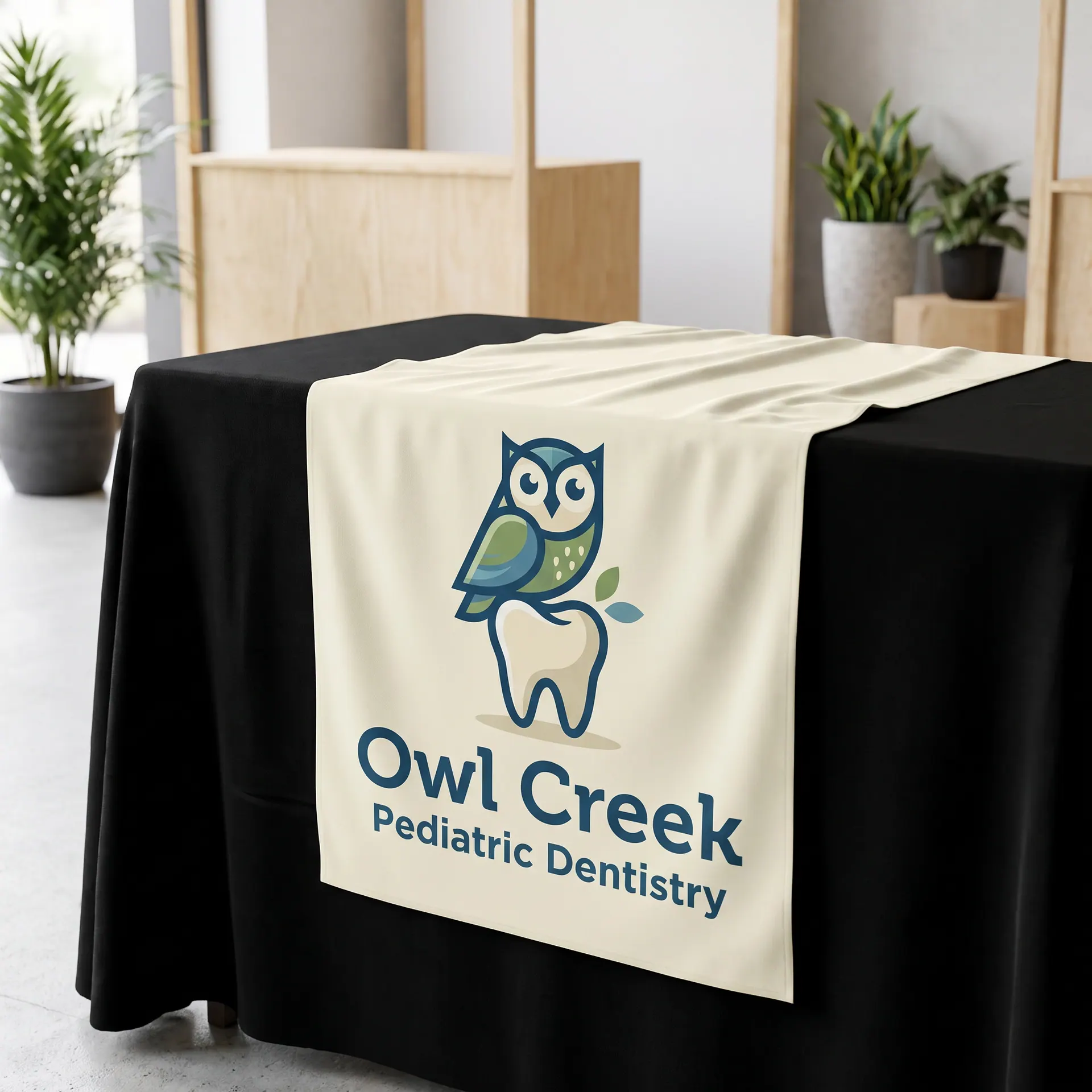 Printed fabric table runner draped over the front of a table with a black tablecloth, shown with a sample design: at a community expo booth